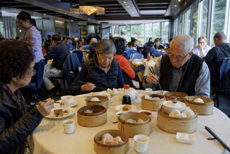A busy dim sum dining room with round tables, steamer baskets and teapots