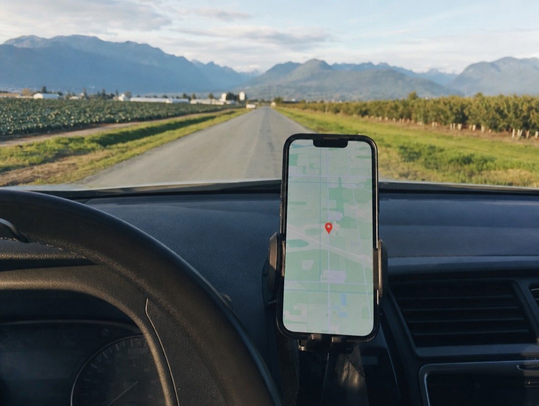 Dashboard-mounted phone guiding a driver toward a pin along a flat farm road