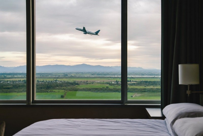 A hotel room window with a plane climbing over flat farmland