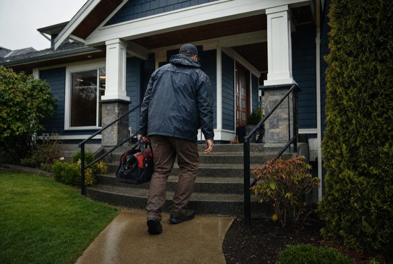 A tradesperson carrying a tool bag to a house in the rain